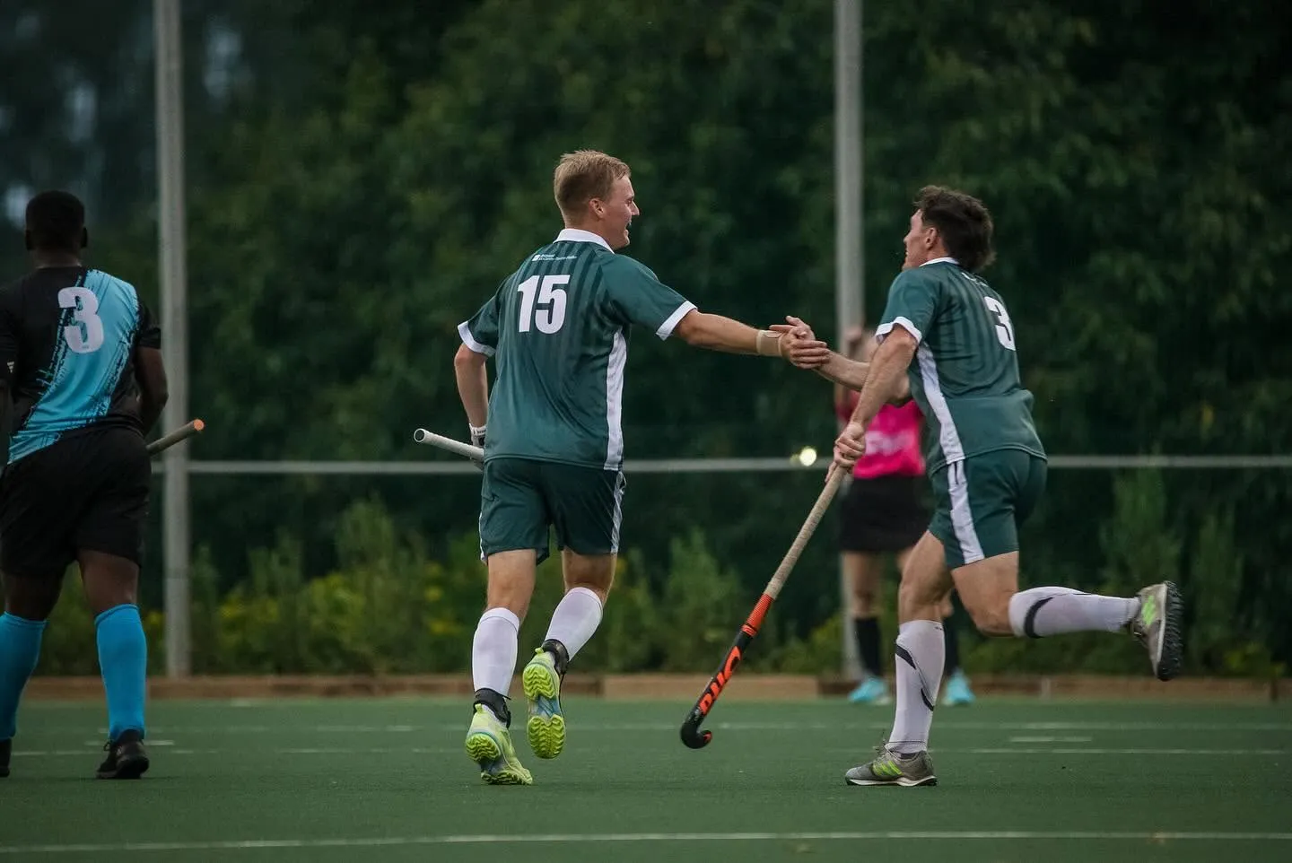 Two Impis men's players in green and white kit shake hands as they jog back after a goal.